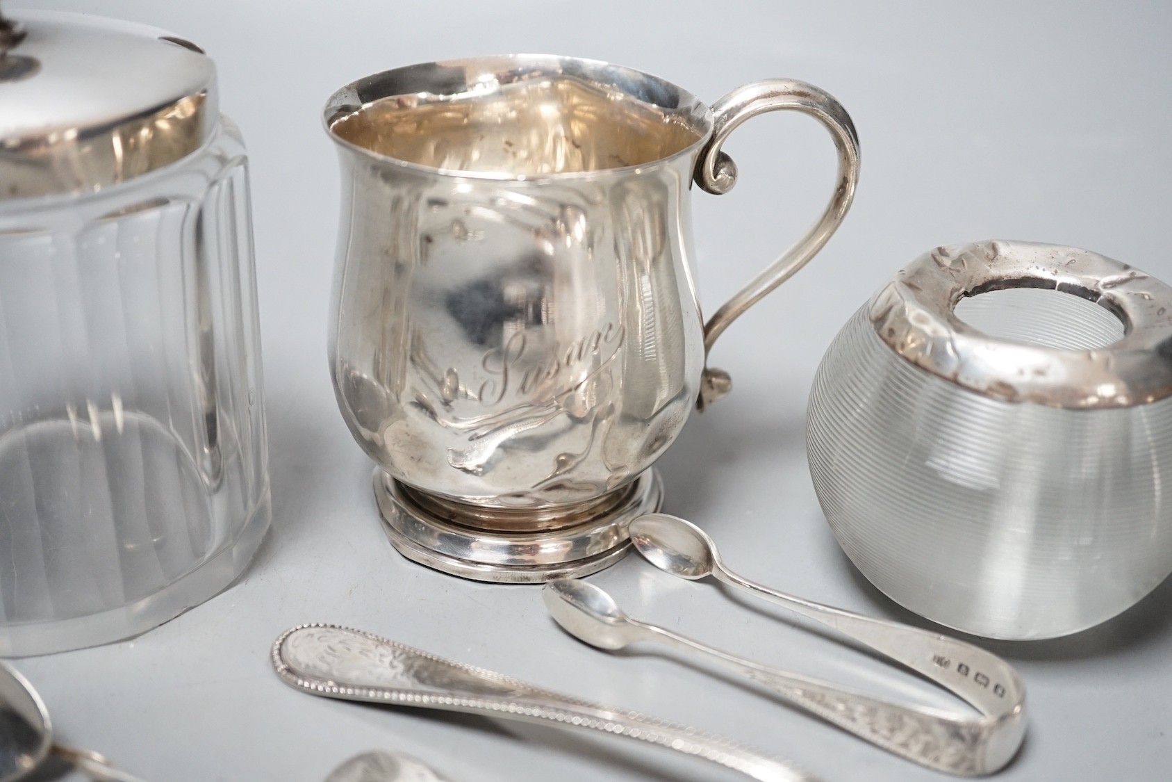 Sundry small silver including a mounted glass match tidy(a.f.), a silver christening mug(a.f.), mounted glass preserve jar, three napkin rings, six items of flatware, thimble T-bar and a sterling bangle.
